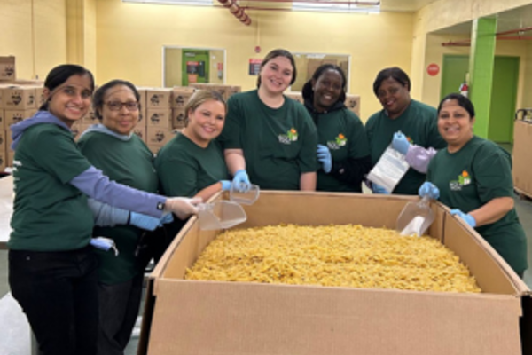 Un grupo de mujeres con camisas verdes sosteniendo una gran caja de pasta