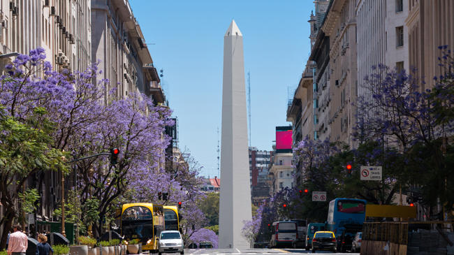 a tall white obelisk on a street with cars and buildings